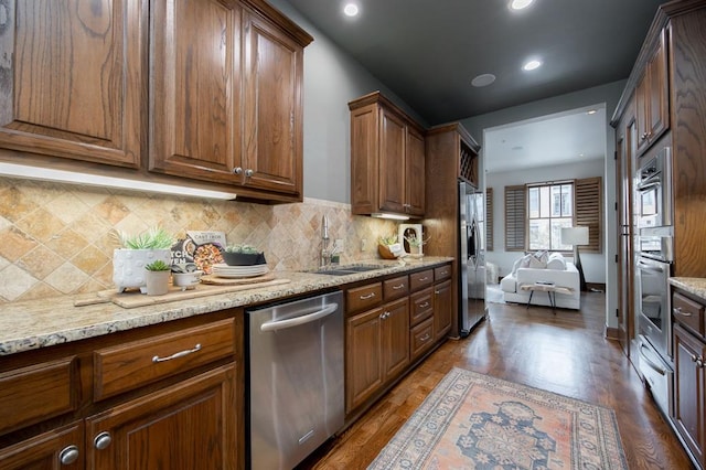 kitchen with sink, stainless steel appliances, light stone counters, hardwood / wood-style floors, and decorative backsplash