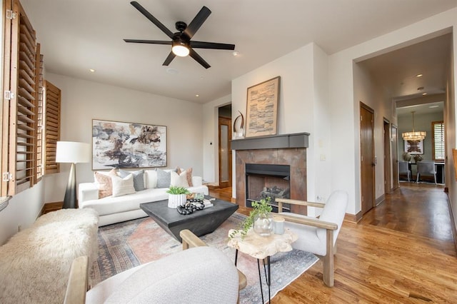 living room featuring ceiling fan with notable chandelier, hardwood / wood-style flooring, and a tiled fireplace