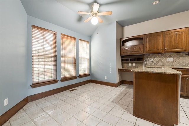 kitchen with lofted ceiling, sink, decorative backsplash, light stone countertops, and light tile patterned floors