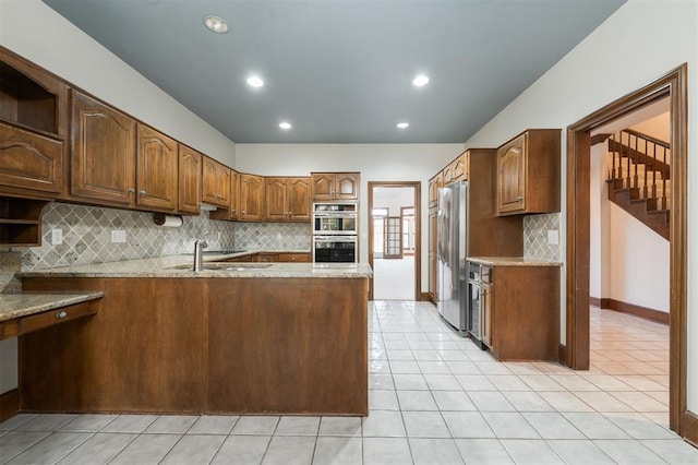 kitchen featuring backsplash, light stone counters, kitchen peninsula, and stainless steel appliances