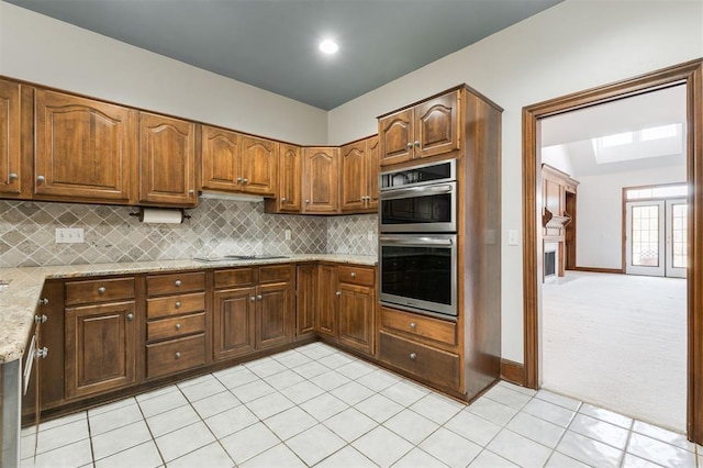 kitchen featuring light carpet, black electric stovetop, tasteful backsplash, light stone counters, and stainless steel double oven