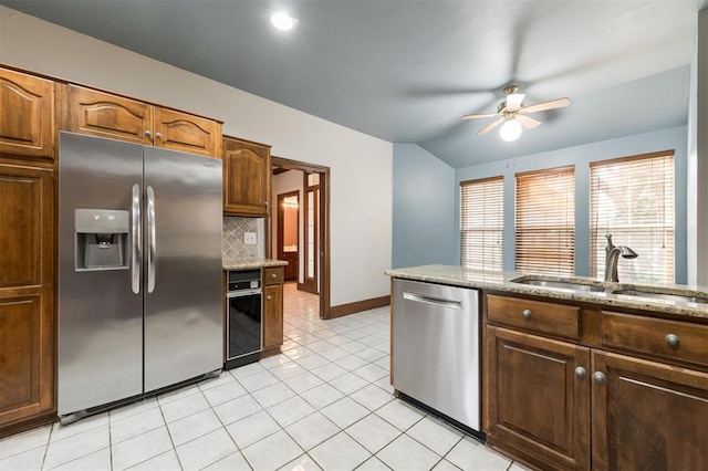 kitchen with ceiling fan, sink, light stone countertops, stainless steel appliances, and tasteful backsplash