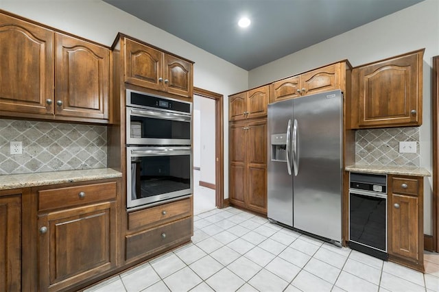 kitchen featuring tasteful backsplash, light stone countertops, light tile patterned floors, and appliances with stainless steel finishes