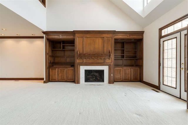 unfurnished living room featuring light carpet, a skylight, high vaulted ceiling, and crown molding