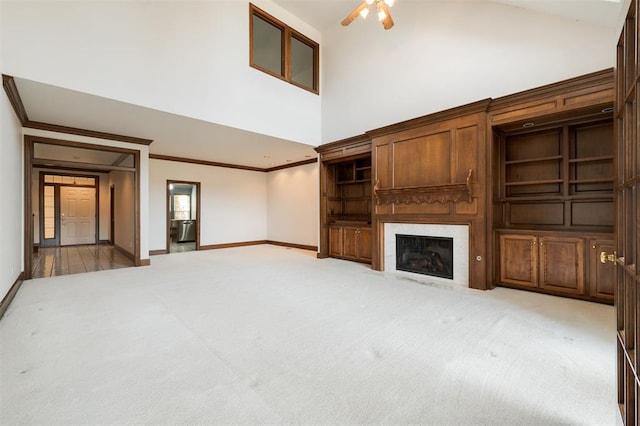 unfurnished living room featuring carpet, a towering ceiling, ceiling fan, and crown molding