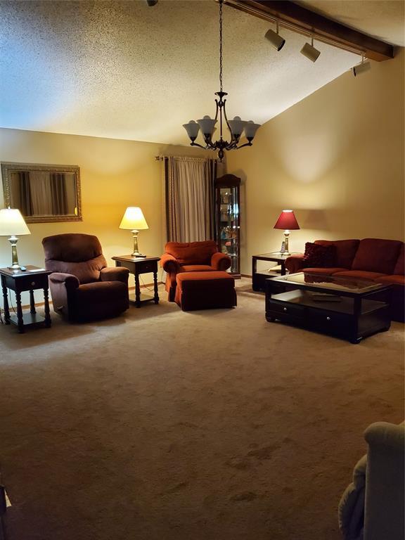 living room featuring rail lighting, an inviting chandelier, lofted ceiling with beams, a textured ceiling, and carpet