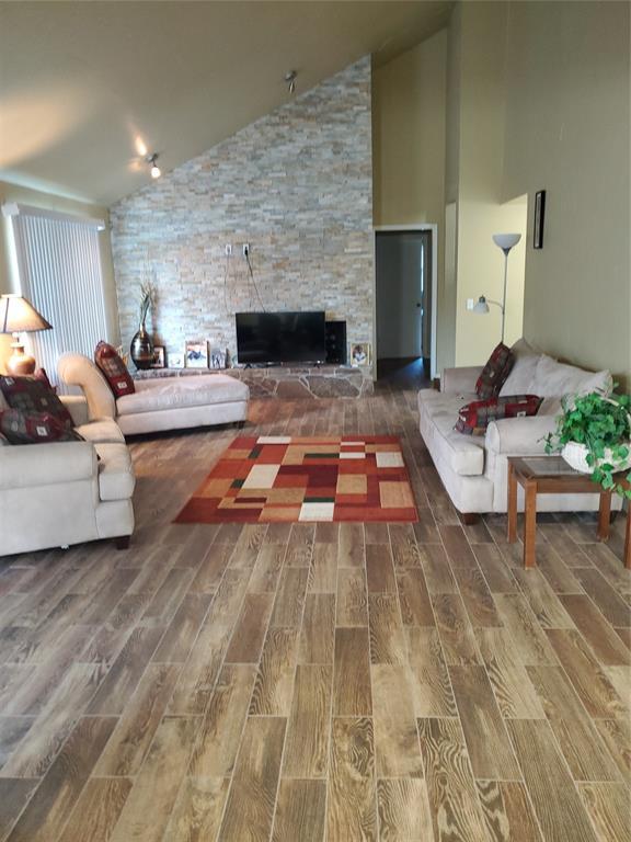 living room with a stone fireplace, hardwood / wood-style floors, and vaulted ceiling