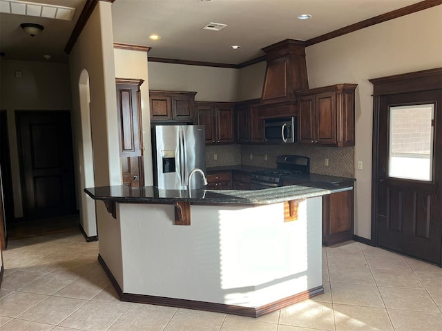 kitchen with dark stone counters, a breakfast bar, stainless steel appliances, crown molding, and light tile patterned floors