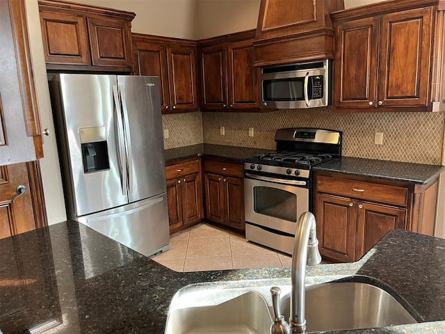 kitchen with backsplash, dark stone counters, sink, light tile patterned floors, and appliances with stainless steel finishes