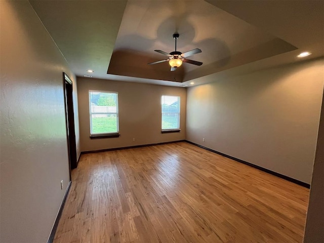 empty room featuring a tray ceiling, ceiling fan, and light hardwood / wood-style floors