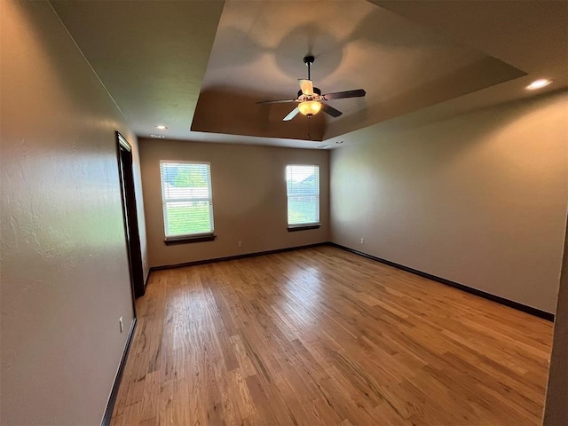 spare room with ceiling fan, light hardwood / wood-style floors, and a tray ceiling