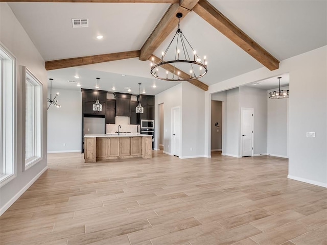 kitchen featuring wall chimney exhaust hood, a notable chandelier, vaulted ceiling with beams, hanging light fixtures, and an island with sink