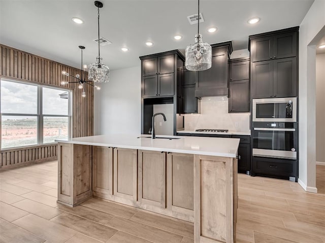 kitchen featuring sink, stainless steel appliances, an island with sink, pendant lighting, and custom range hood