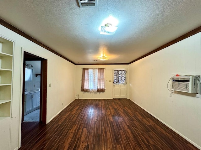 spare room featuring a textured ceiling, crown molding, a wall mounted air conditioner, and dark wood-type flooring