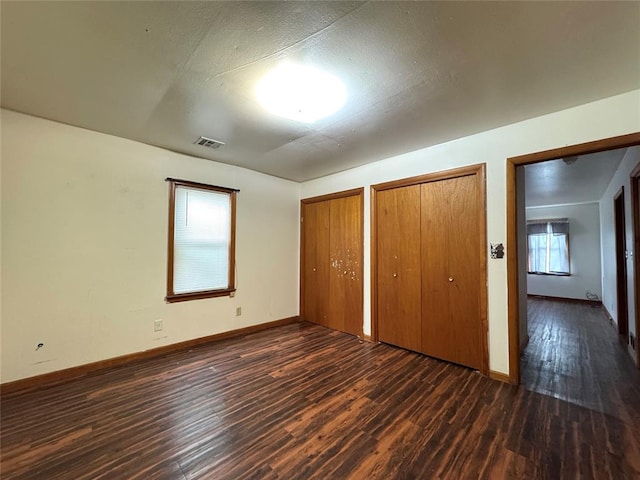 unfurnished bedroom with a textured ceiling, dark hardwood / wood-style flooring, and two closets