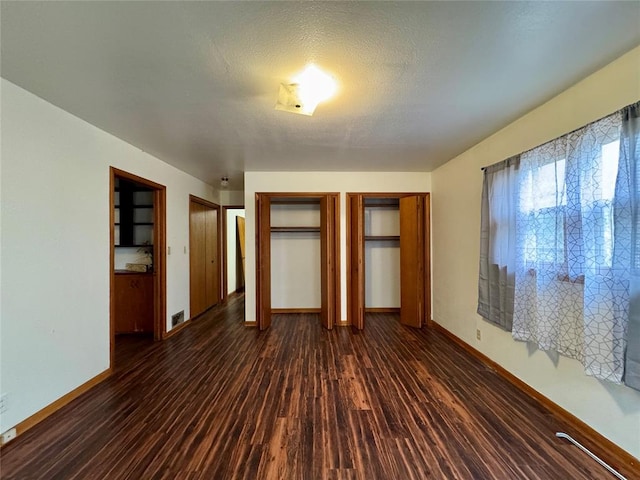 unfurnished bedroom with two closets, dark hardwood / wood-style flooring, and a textured ceiling