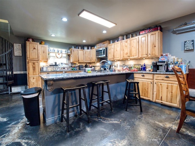 kitchen featuring kitchen peninsula, a breakfast bar, dark stone countertops, and light brown cabinetry