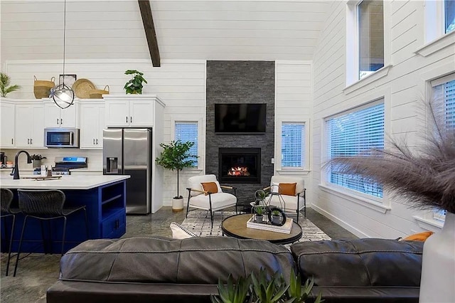 living room with a stone fireplace, sink, high vaulted ceiling, and beamed ceiling