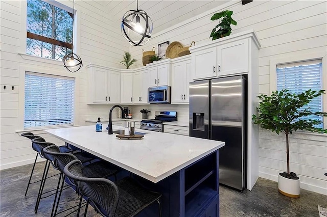 kitchen with a center island with sink, white cabinets, stainless steel appliances, and decorative light fixtures