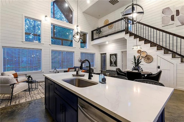 kitchen featuring stainless steel dishwasher, sink, decorative light fixtures, high vaulted ceiling, and an island with sink