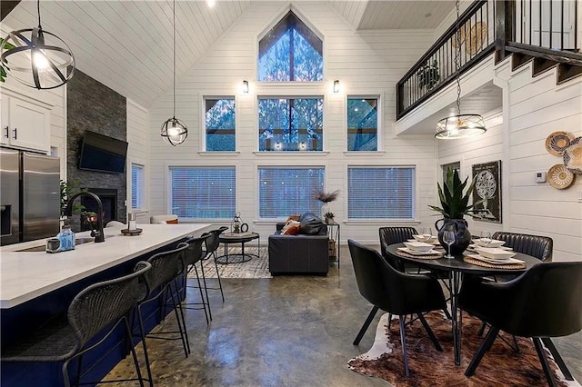 dining area with wood ceiling, wooden walls, an inviting chandelier, high vaulted ceiling, and a fireplace