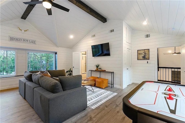 living room featuring ceiling fan, beamed ceiling, high vaulted ceiling, wood walls, and light hardwood / wood-style floors