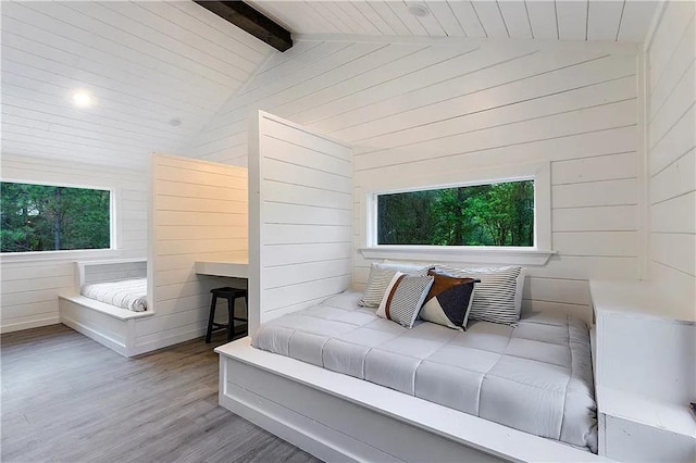 bedroom featuring vaulted ceiling with beams, light wood-type flooring, and wooden walls