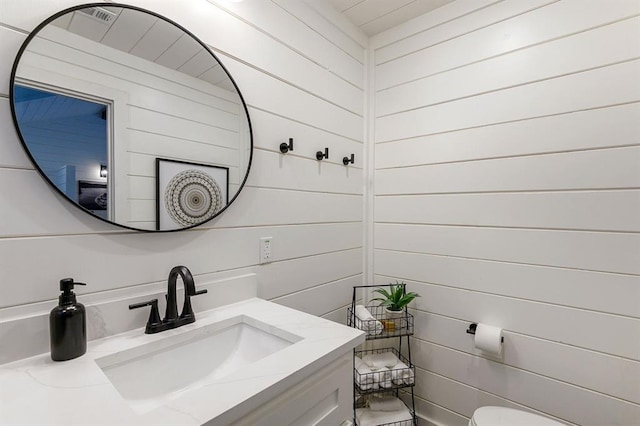 bathroom featuring vanity, toilet, and wood walls