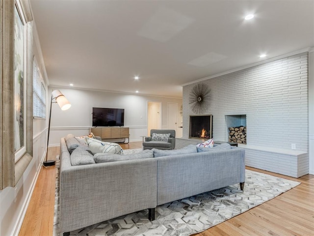 living room with light wood-type flooring, ornamental molding, and a brick fireplace