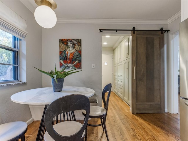 dining area featuring light wood-type flooring, a barn door, and crown molding