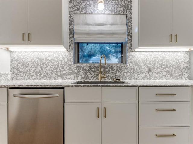 kitchen with stainless steel dishwasher, white cabinets, light stone countertops, and sink