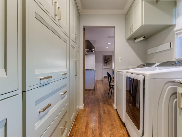 laundry room featuring ornamental molding, washer and clothes dryer, cabinets, and wood-type flooring