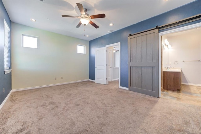 unfurnished bedroom featuring a barn door, ceiling fan, ensuite bath, and multiple windows