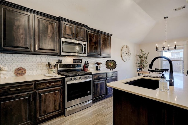 kitchen featuring vaulted ceiling, backsplash, hanging light fixtures, stainless steel appliances, and light hardwood / wood-style flooring