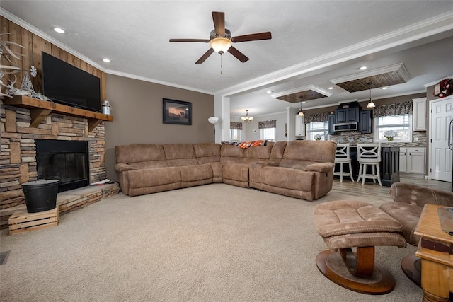 carpeted living room with ornamental molding, a stone fireplace, and ceiling fan