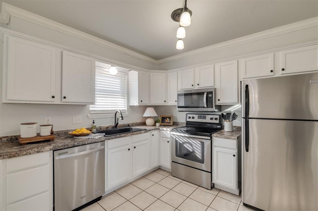 kitchen with dark stone counters, sink, ornamental molding, white cabinetry, and stainless steel appliances