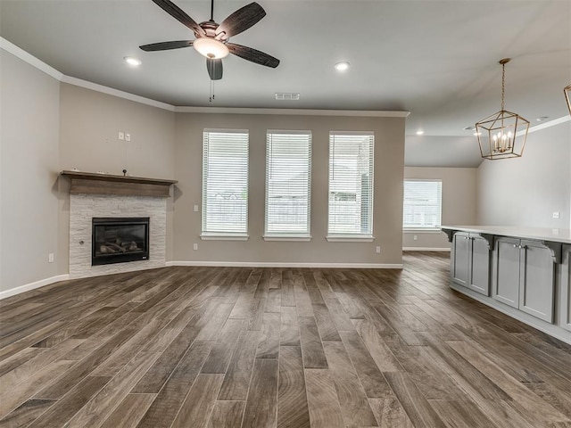 unfurnished living room featuring visible vents, ceiling fan with notable chandelier, dark wood-style floors, and ornamental molding