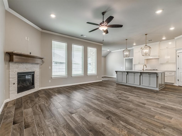 unfurnished living room featuring a stone fireplace, crown molding, a ceiling fan, and dark wood-style flooring