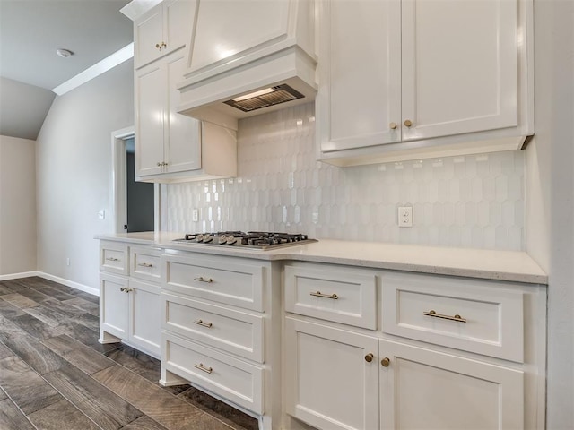 kitchen featuring baseboards, stainless steel gas cooktop, custom exhaust hood, white cabinets, and backsplash