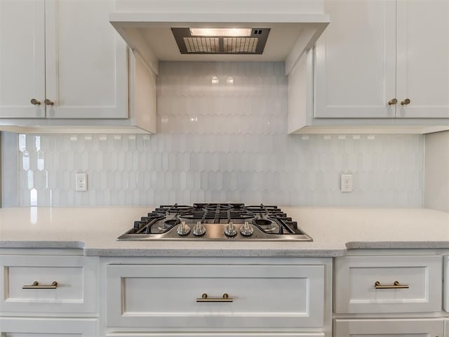 kitchen featuring light stone counters, backsplash, stainless steel gas stovetop, white cabinets, and extractor fan