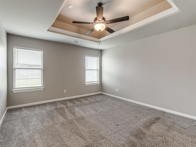 carpeted spare room featuring a raised ceiling, visible vents, baseboards, and ceiling fan