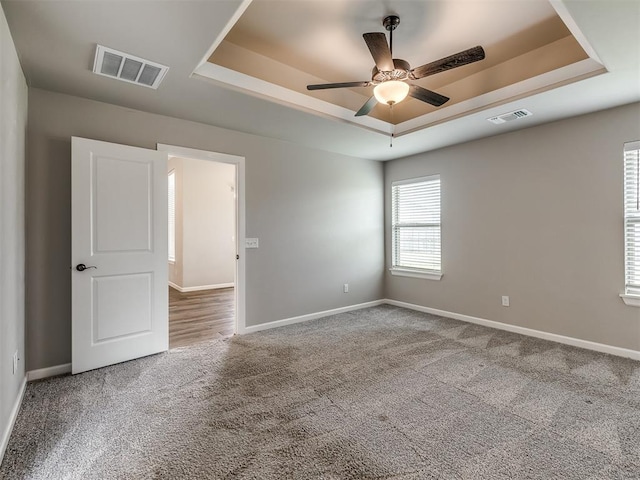 empty room featuring visible vents, a raised ceiling, and carpet