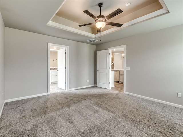 unfurnished bedroom featuring baseboards, visible vents, ensuite bath, a tray ceiling, and light carpet