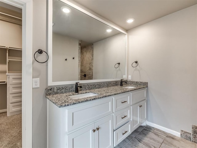 full bathroom featuring a sink, baseboards, double vanity, and a spacious closet