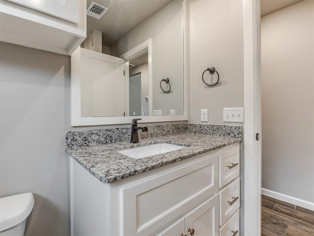 bathroom featuring visible vents, baseboards, toilet, wood finished floors, and vanity