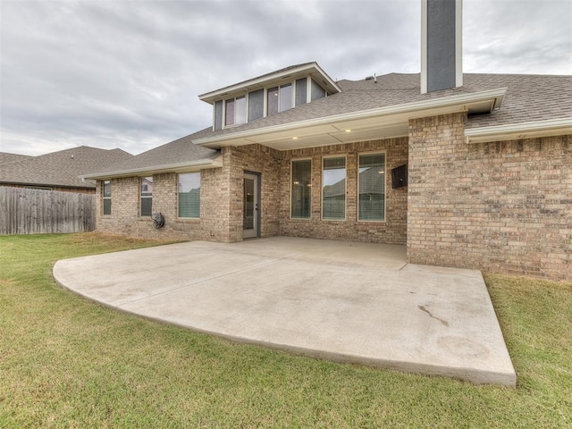 back of house with fence, a yard, a shingled roof, brick siding, and a patio area