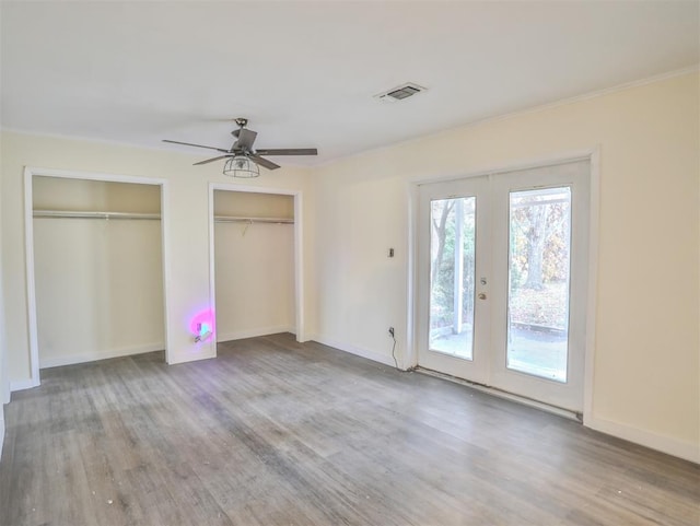 unfurnished bedroom featuring ceiling fan, french doors, hardwood / wood-style floors, access to outside, and two closets