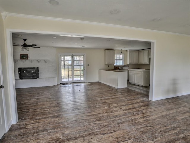 unfurnished living room with dark hardwood / wood-style floors, ceiling fan, crown molding, and a brick fireplace