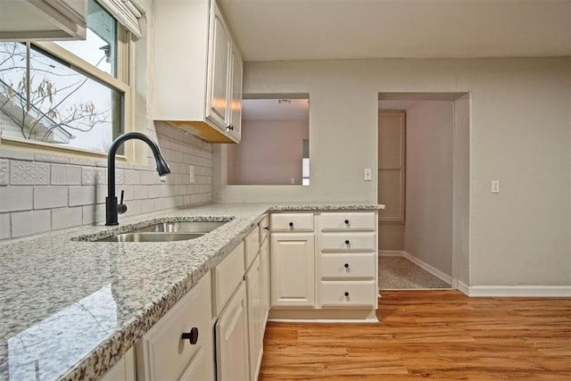 kitchen with tasteful backsplash, white cabinetry, sink, and light wood-type flooring