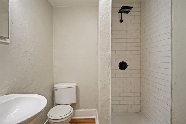 bathroom featuring tiled shower, toilet, and sink